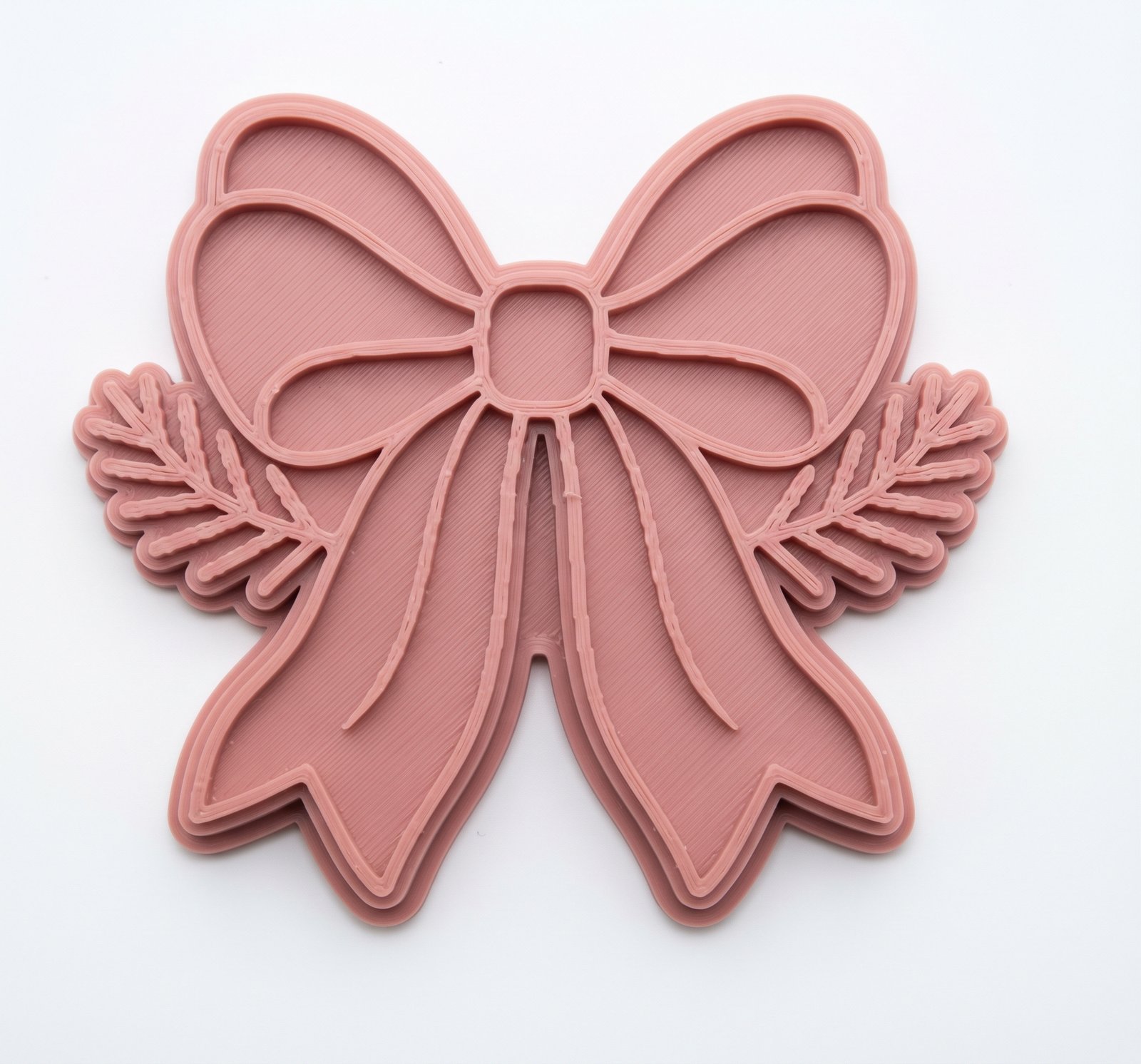 Cortador e marcador plástico em tom rosa antigo com formato de laço central e ramos de folhas nas laterais, visto de cima sobre fundo branco.