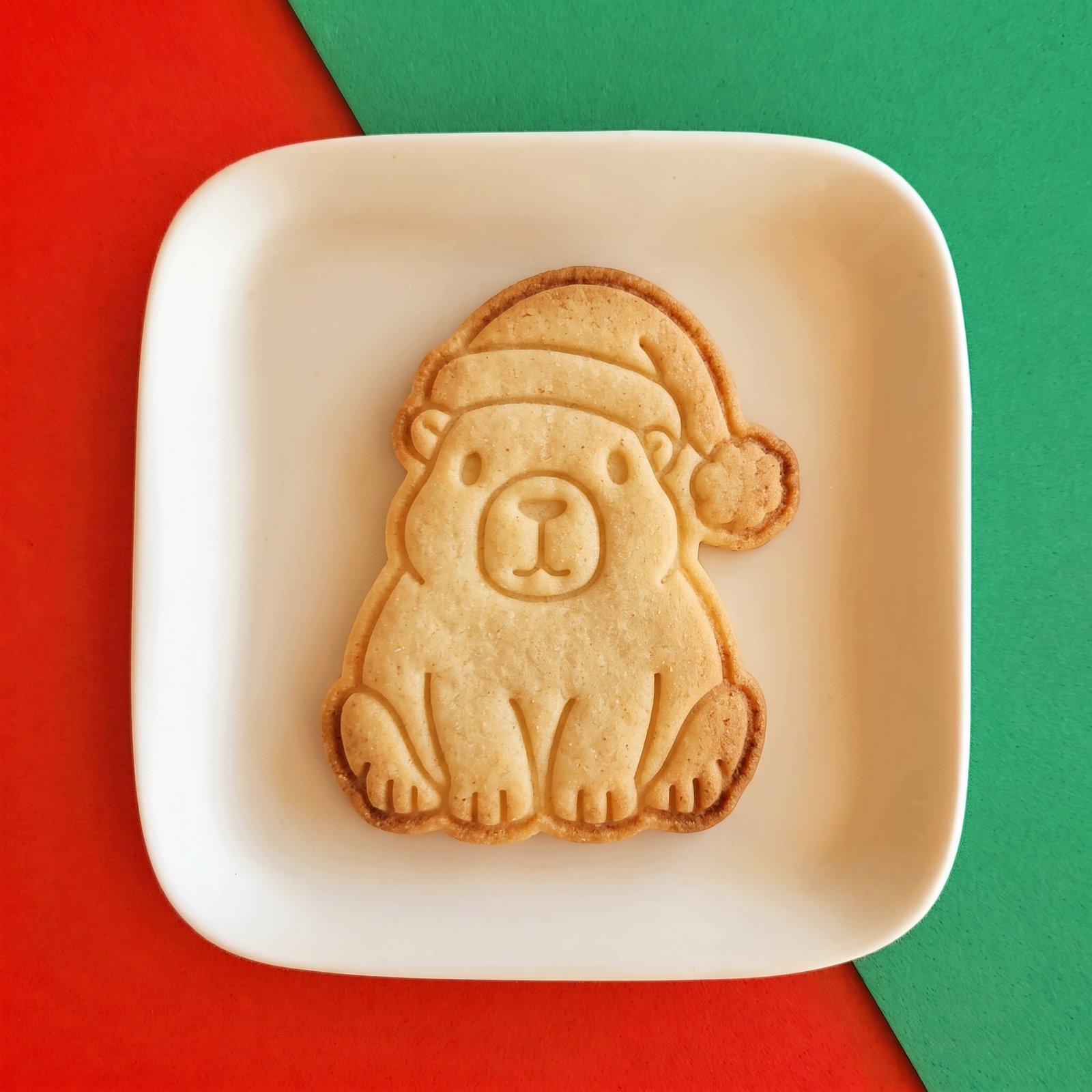 Biscoito assado decorado no formato de capivara usando gorro de Papai Noel sobre um prato branco.